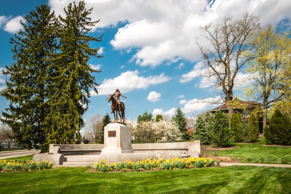 Bronze statue of Native American sitting on a horse with arms stretched out to his sides and face looking up.